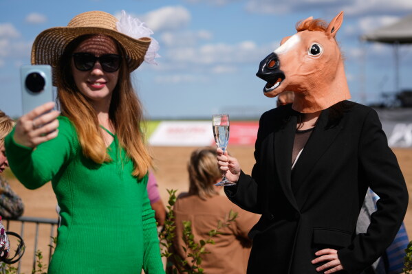 An attendee wearing a horse head mask strikes a pose at the annual festival honoring the Orlov Trotter breed outside Tarusa, Kaluga region, Russia, Saturday, Aug. 15, 2026. (AP Photo/Pavel Bednyakov)