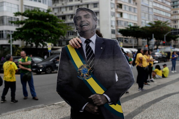 A supporter of opposition presidential candidate Flavio Bolsonaro carries an image of Flavio Bolsonaro's father, former President Jair Bolsonaro, as he arrives for a campaign rally in Rio de Janeiro, Brazil, Sunday, Aug. 16, 2026. (AP Photo/Bruna Prado)