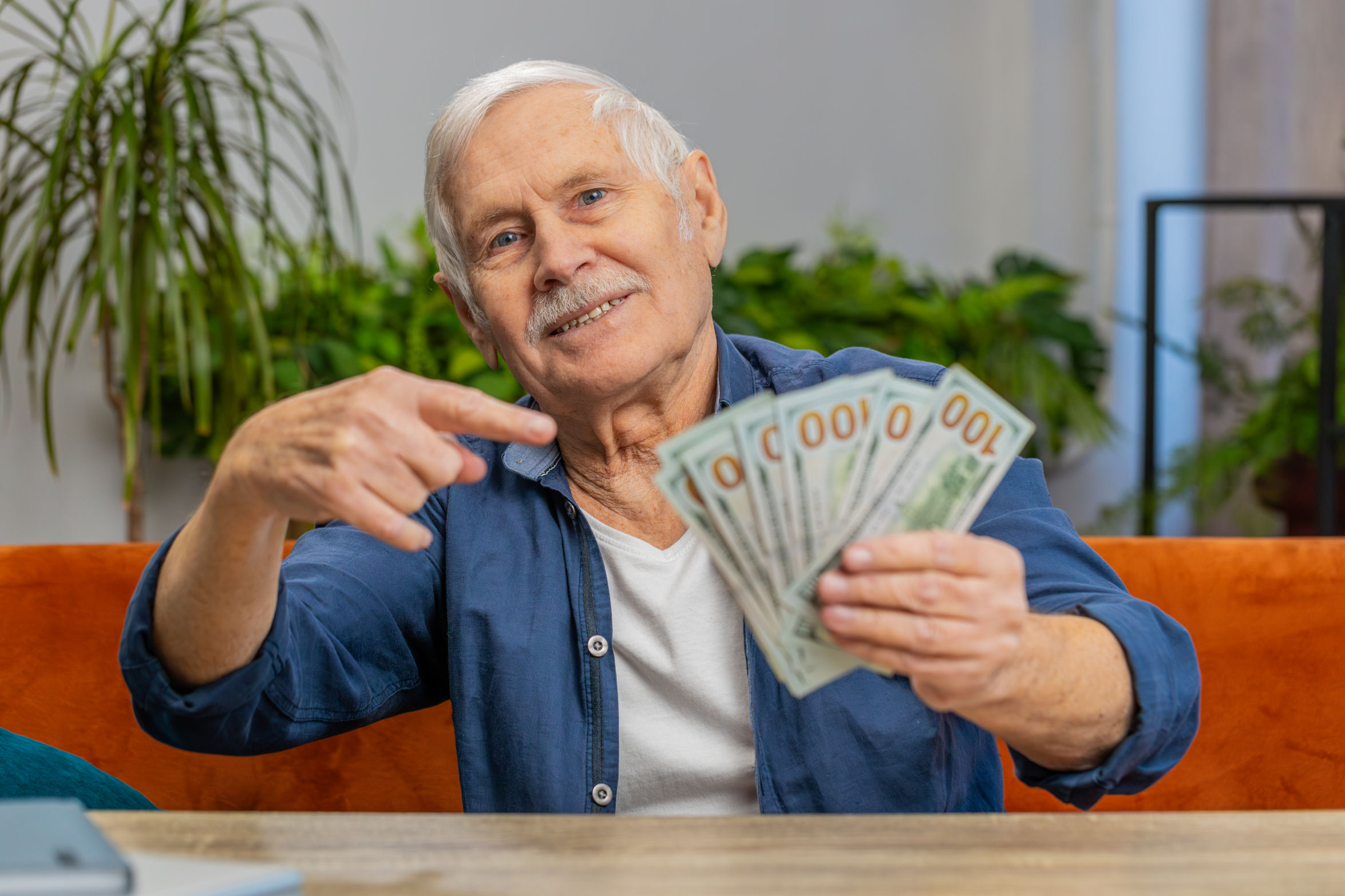 A retired investor is holding several $100 bills, fanned out in his hand.