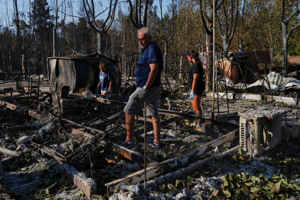 Maria del Carmen, left, her daughter Maria del Carmen Lopez, right, and her partner Mario Gonzalez, center, collect their belongings after their bungalows were ravaged by a wildfire at a campsite in Valle de Iruelas, Spain, July 30, 2026. (AP Photo/Manu Fernandez, File)