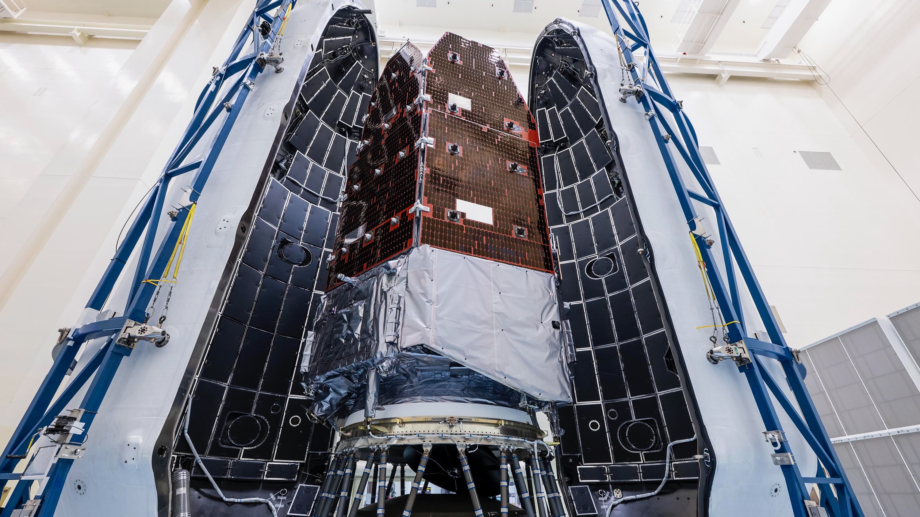 A tall structure with solar panels within a large white capsule that's yet to close.