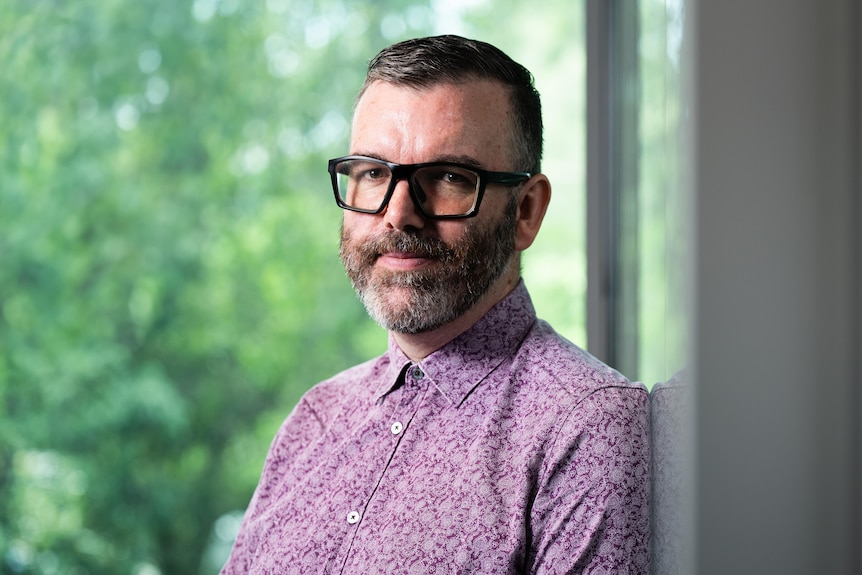 A man in purple collared shirt with a beard and glassed.
