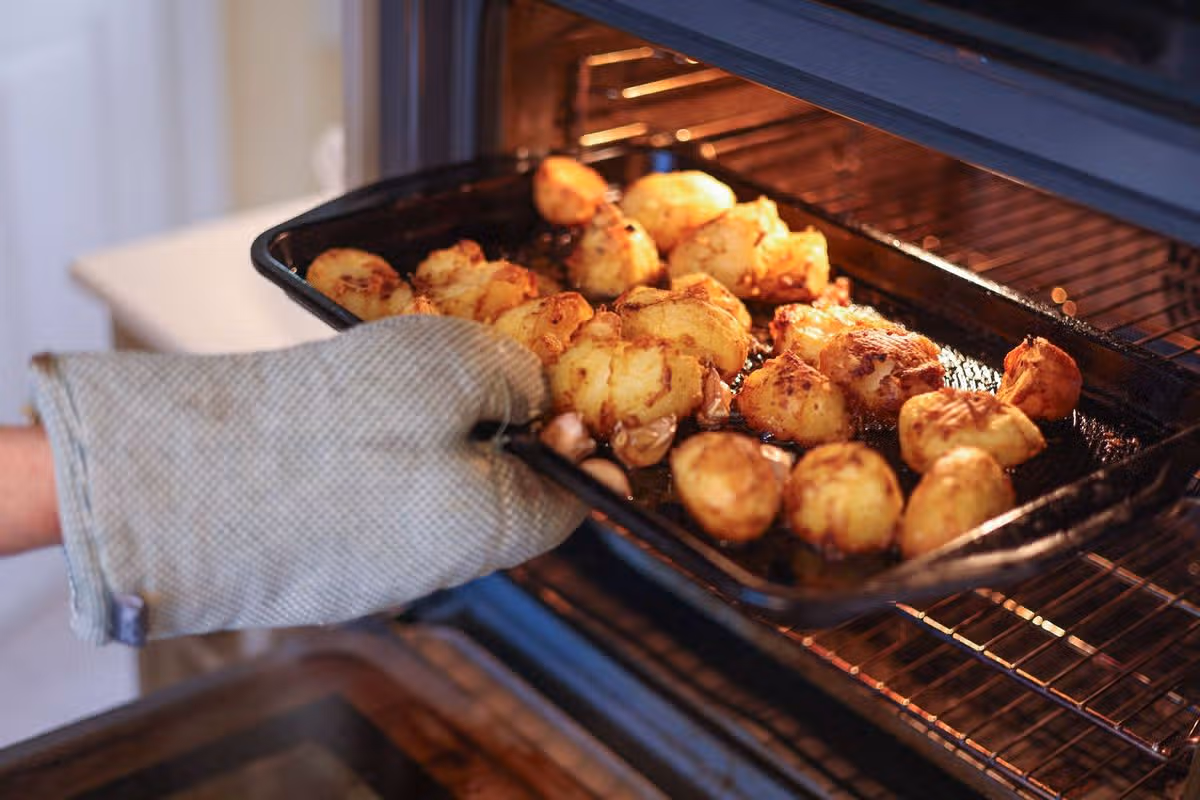 Taking hot crispy roast potatoes out of a domestic oven with an oven mitt