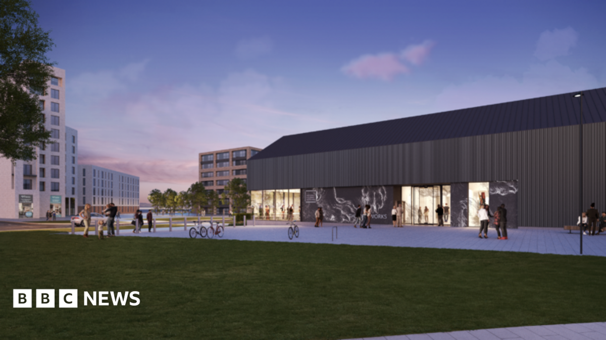 An artist's impression of the future Art Works development in Granton, showing a render of a building with a sloping roof, brown frontage and bright lights on inside and people walking near a patch of grass.