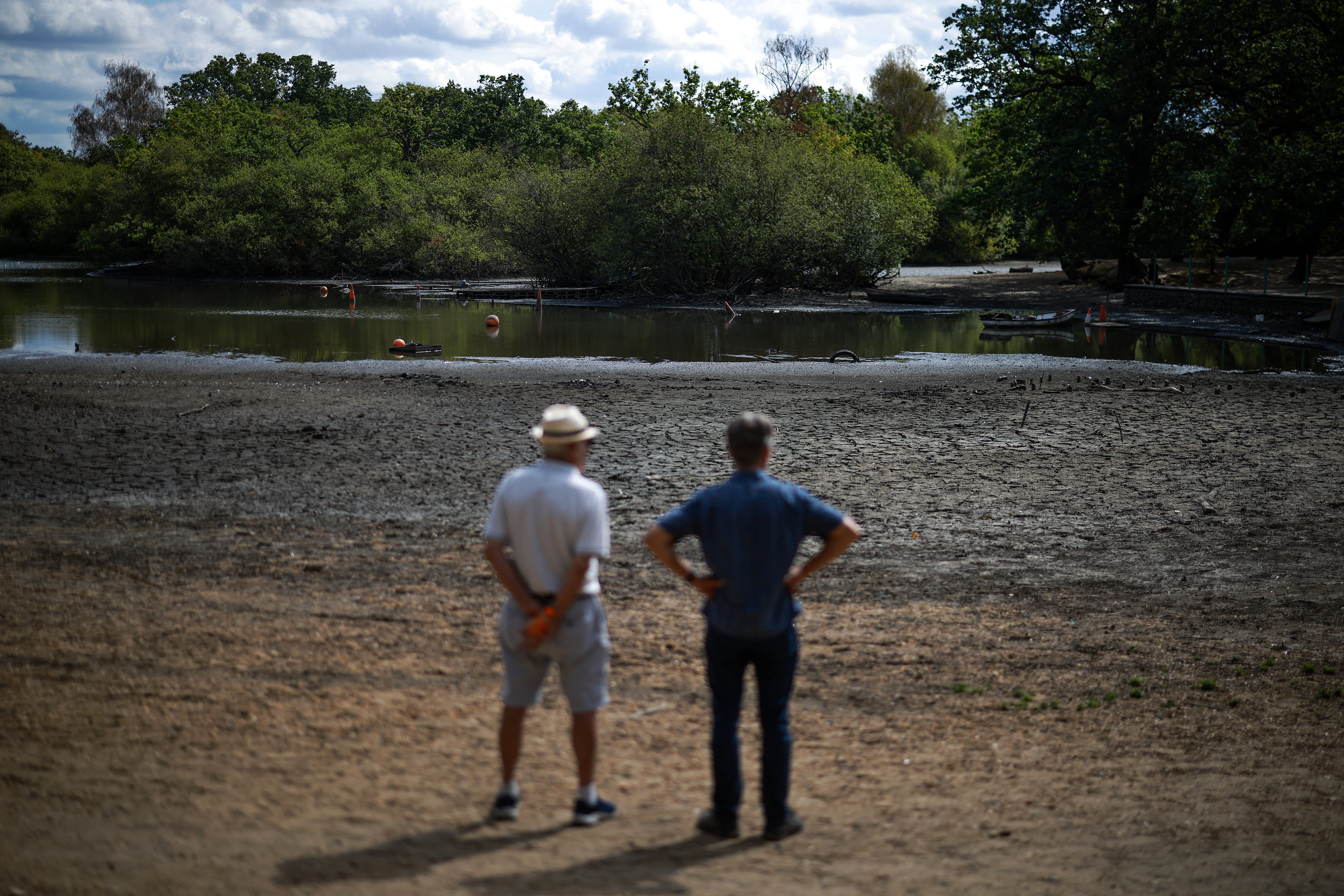 People look out over the dried and cracked bed of the depleted Hollow Pond and Leyton flats near Wanstead, east London