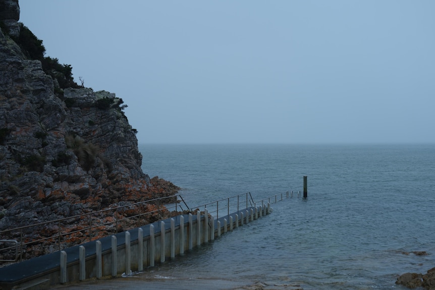 A rocky cliffside and jetty, looking out to the water on a foggy day.