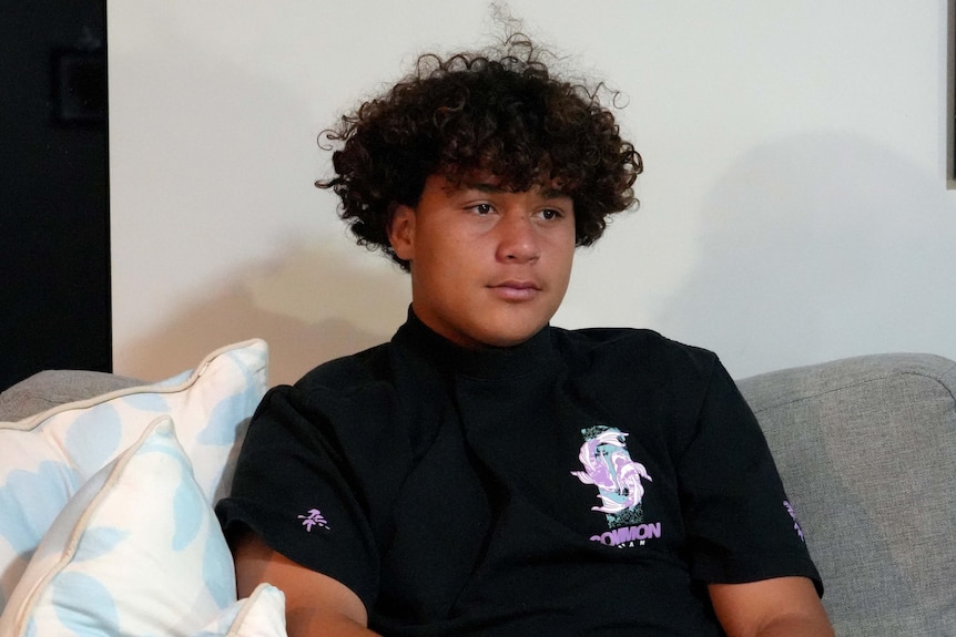 A young boy with dark curly hair sits on a couch. 