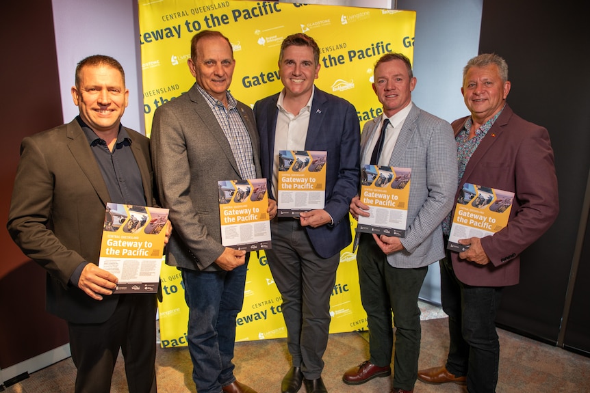Five central Queensland mayors stand smiling with 'Gateway to the Pacific' booklets, in front of a banner at a launch event.