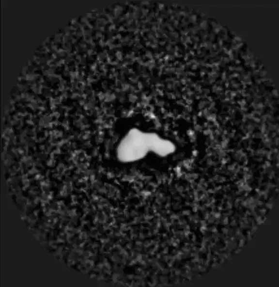 A lumpy white rock on a dark grainy background spins and one brighter dot at upper left circling it.