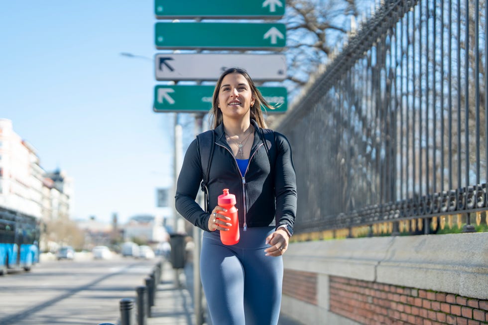 Young woman walking city street carrying water bottle Young woman walking city street carrying water bottle