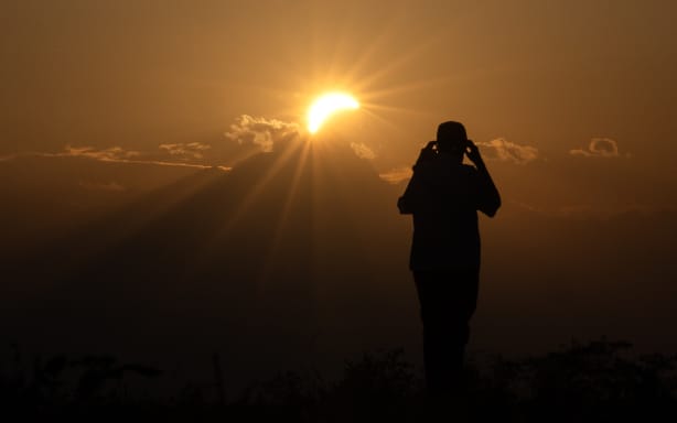 A man watches the moon pass over the sun's horizon near the Monviso mountain during a partial solar eclipse in in Bene Vagienna, near Turin, northwestern Italy, on August 12, 2026. The eclipse was mainland Europe's first total eclipse since 2006. Throughout human history eclipses have stirred amazement, fear and reverence, as they appear to momentarily halt the normal course of nature, creating a strange twilight during which temperatures drop, shadows appear at strange angles and some animals go to sleep. (Photo by Marco Bertorello / AFP)