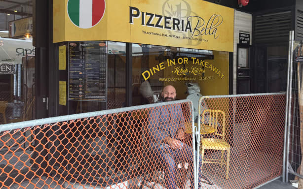 Pizzeria Bella owner Yusef Corten sits in front of his restaurant and behind a fence while work is done on Bridge Street.