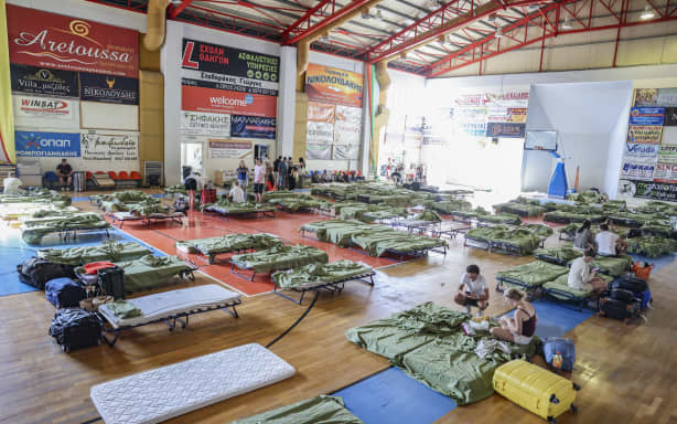 Tourists and local residents from the resort village of Agia Galini gather in an indoor stadium where they are temporarily accommodated during a wildfire in Rethymno area, in the southwest of the Greek island of Crete on July 30, 2026. Thousands of people were evacuated late on July 29, 2026, as fires threatened a tourist resort on the Greek island of Crete and continued to rage on July 30, fanned by violent winds, a local official said. The evacuations were decided as the fire, which broke out on July 29 and had earlier killed two firefighters, got to within a kilometre of the village before changing direction in the evening. (Photo by Costas METAXAKIS / AFP)