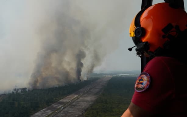 This aerial view taken from a Civil Security helicopter shows a crew member looking at firefighting vehicles lined up along a road working to suppress a wildfire near Ares, southwestern France, on July 28, 2026. (Photo by Baz Ratner / POOL / AFP)
