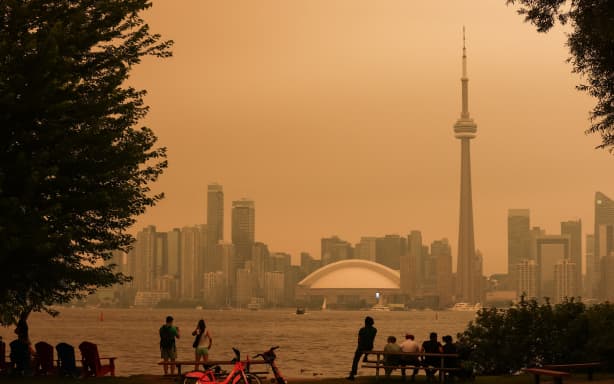 People look toward the downtown skyline from the Toronto Islands as forest fires in Northern Ontario cause poor air quality over the city, in Toronto, Ontario, Canada, July 15, 2026. Toronto had the worst air quality of any major city in the world on Wednesday, the Swiss firm IQAir said, as Canadian authorities urged people to stay indoors. Toronto edged out New Delhi and the Democratic Republic of Congo's capital Kinshasa as wildfire smoke turned the skies a hazy yellowish-grey in Canada's largest city. (Photo by Cole BURSTON / AFP)