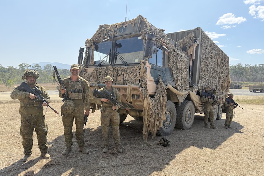 Three army personnel standing in front of a large army vehicle
