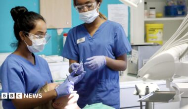 Young female dentist and assistant working on female patient in chair