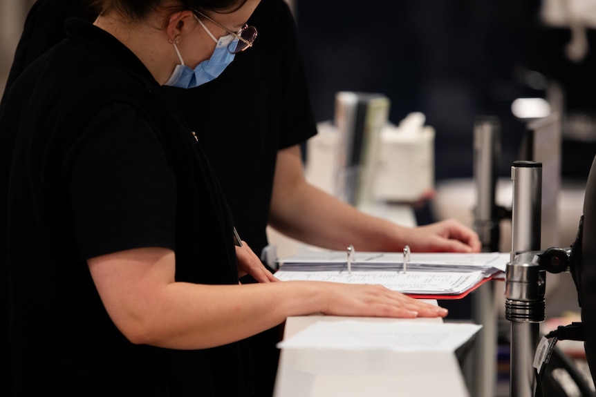 Two unidentified nurses look at paperwork in a file.