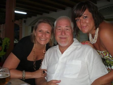 Natalie and Danielle stand either side of Pete, who is sitting at a table
