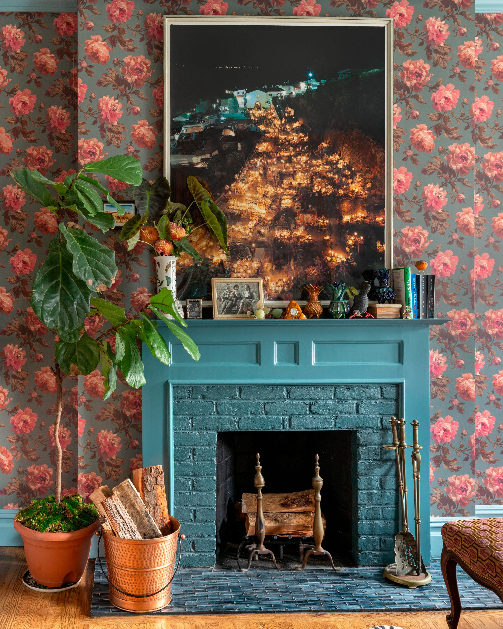 Bedroom with floral wallpaper, a green fireplace mantle, plants, and a large framed night photo above the fireplace. Bedroom with floral wallpaper, a green fireplace mantle, plants, and a large framed night photo above the fireplace.