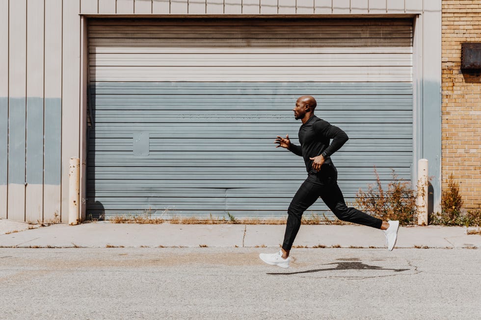 Side view of man jogging in city Person running on an urban street wearing black athletic clothing and white shoes.