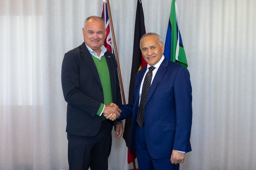 Two men shake hands in front of flags
