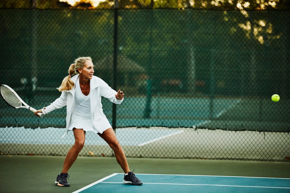 mature woman preparing to hit return while warming up for early morning tennis match