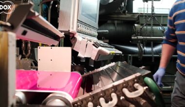 A person wearing blue gloves and a striped sweater operates industrial machinery processing a bright pink material.