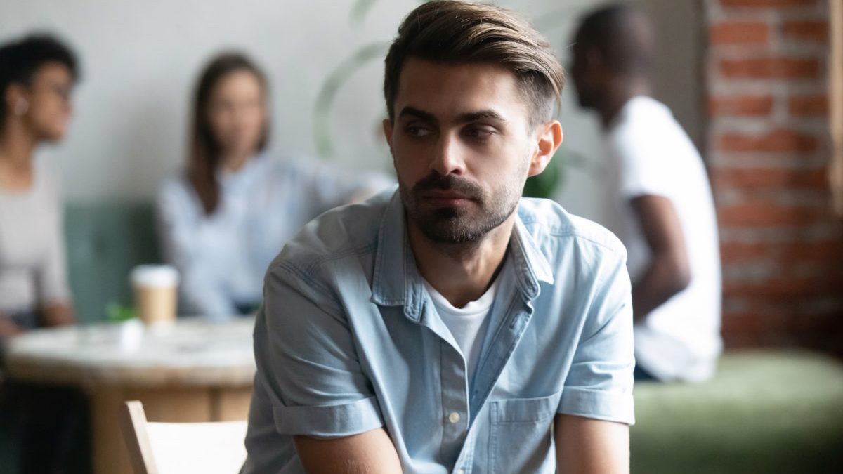 Frustrated lonely shy guy sitting apart of others teenagers - stock photo