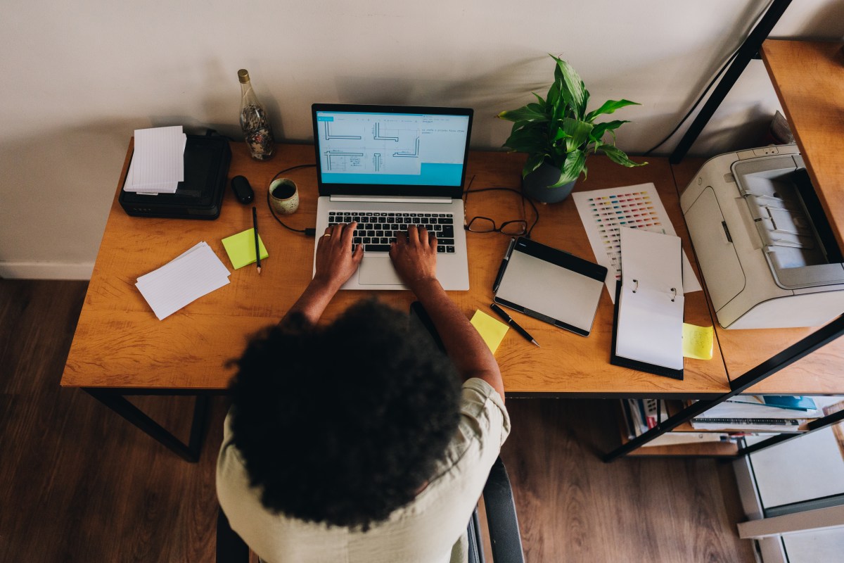 Overhead view of a woman working on a laptop while sitting at a cluttered desk