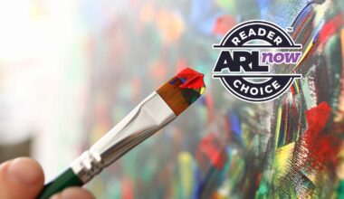 Close-up of a paintbrush with red, yellow and blue paint, painting a vibrant canvas, with a circular 'Reader’s Choice AR Now' badge in the upper right.