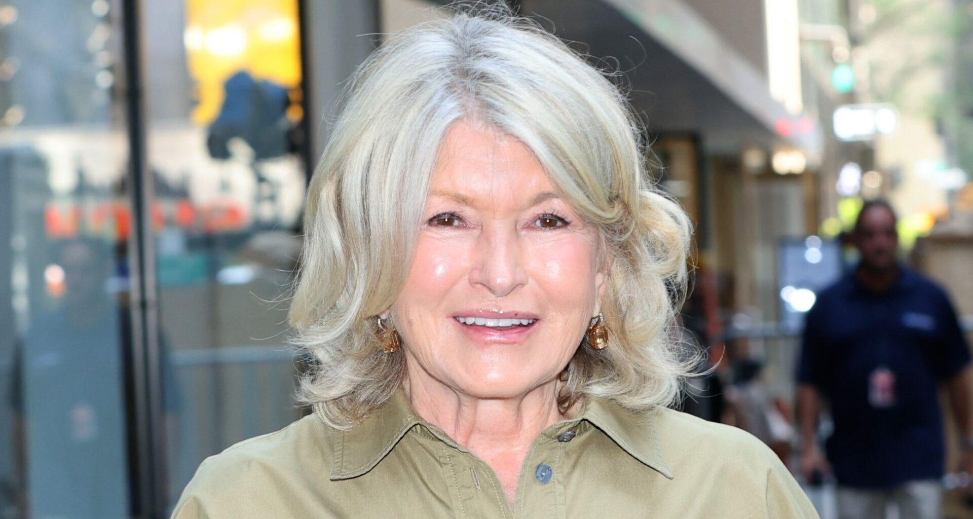 Image of Martha Stewart smiling with blonde curled shoulder-length bob and wearing a khaki beige shirt