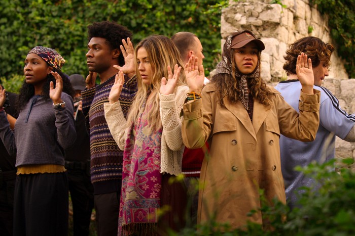 Outer_Banks_n_S5_E3_00_00_26_03R Carlacia Grant as Cleo, Jonathan Daviss as Pope, Madelyn Cline as Sarah Cameron, Drew Starkey as Rafe, Madison Bailey as Kiara and Chase Stokes as John B in Outer Banks. They are stood outside in a circle facing out with their hands up.