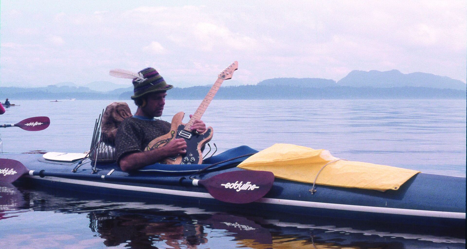 Jim Nollman playing electric guitar in a modified kayak.