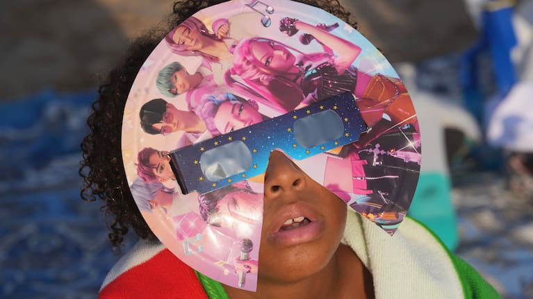 A beachgoer wearing special eclipse glasses looks up during the beginning phase of a solar eclipse at Puerto de Sagunto beach near Valencia, Spain.