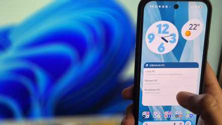 A hand holding a Pixel 10 with the thumb hovering over a shutdown button on the home screen and a Windows PC in front of it.