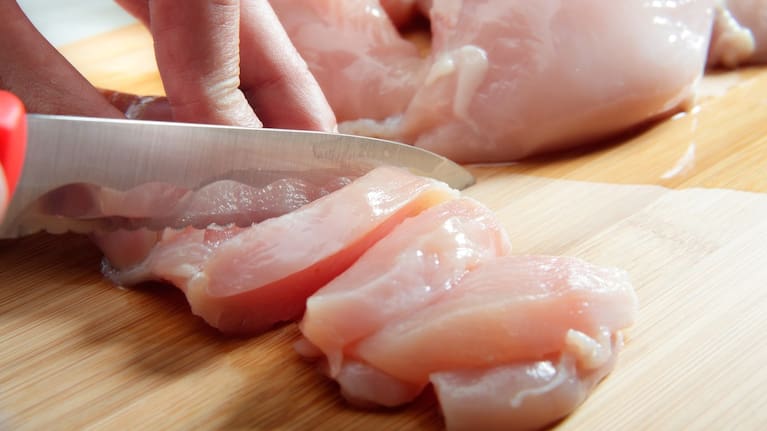 A person cuts raw chicken on a chopping board (file image).