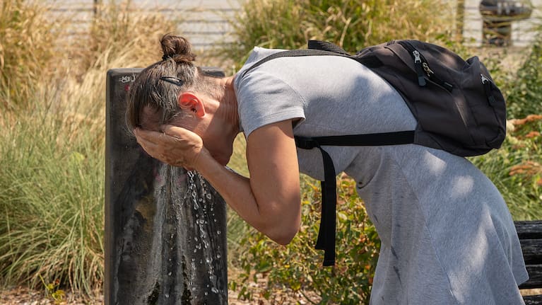 A woman splashes water on her face at a public fountain on a hot day in Bordeaux, France.