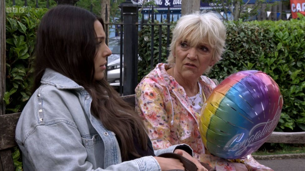 EastEnders Priya Nandra-Hart and Jean Slater eastenders priya nandra hart and jean slater sitting on a bench in the square gardens, with jean holding a multi coloured balloon