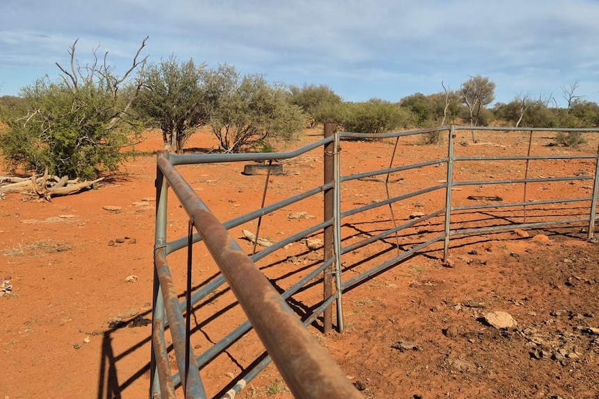 A line of steel fencing on orange dirt, with several bent bars.