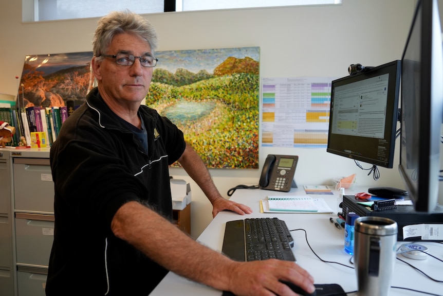 A man stands in front of his desk