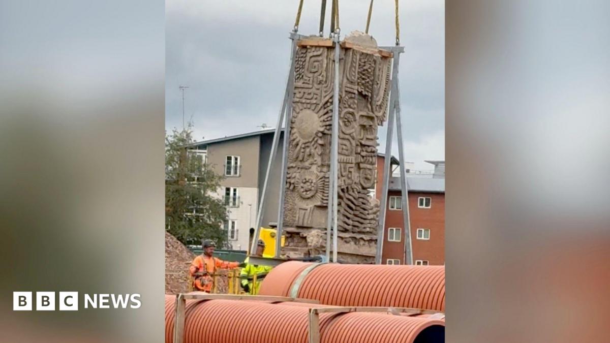 A close-up of the Aztec-style mural being lifted up by metal cranes.