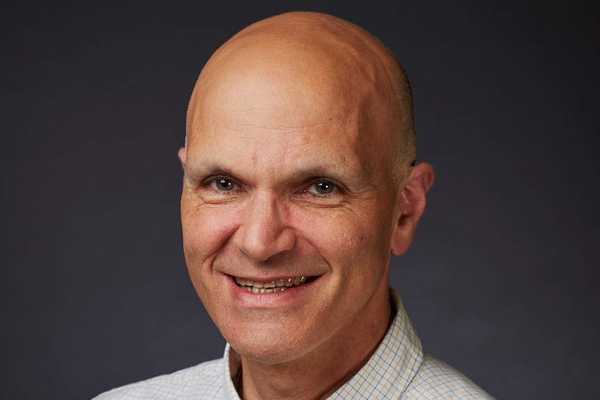 Emery Schubert, from shoulders up, is bald and wears white shirt. He smiles widely.