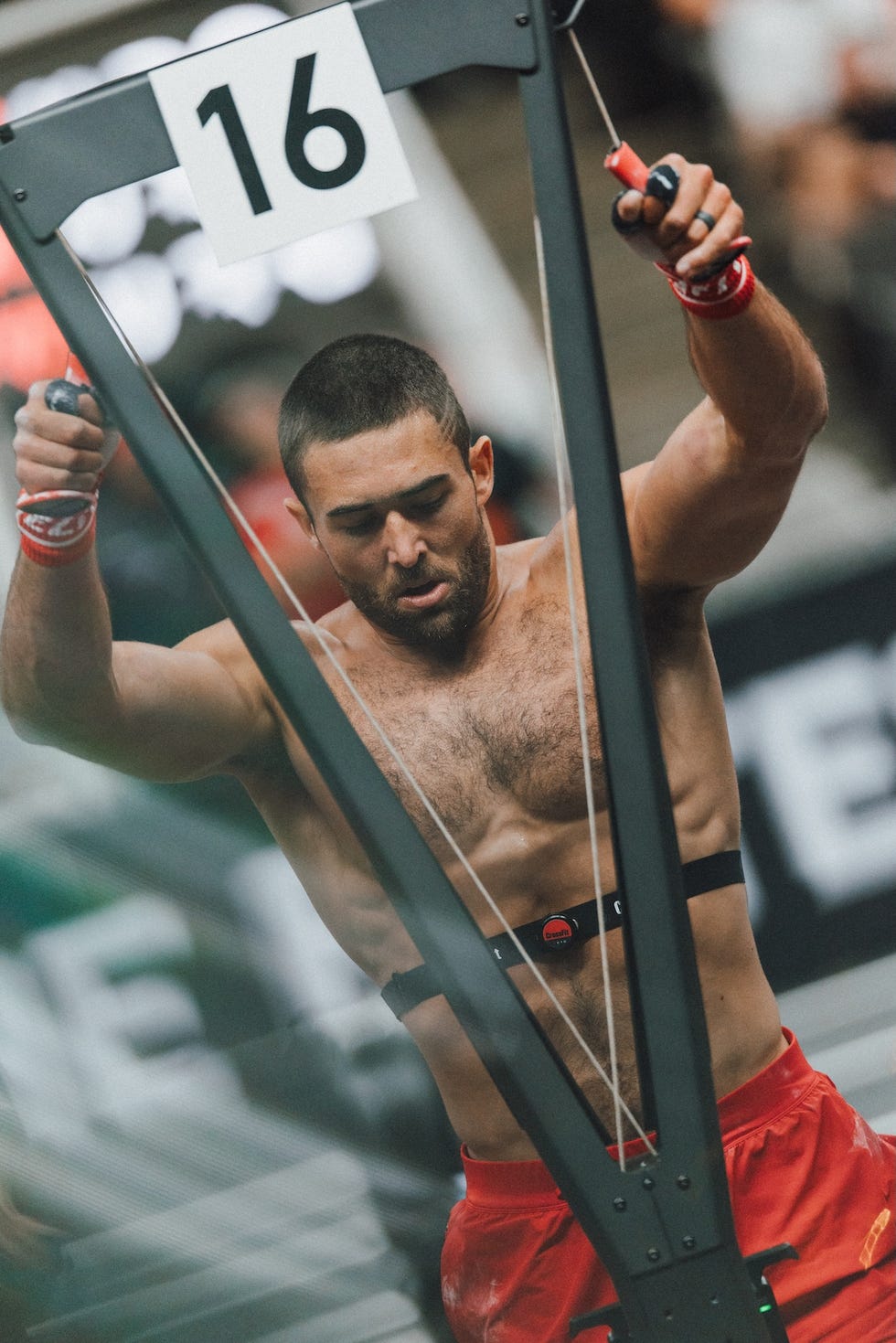 Athlete performing a fitness exercise on a machine, focused and wearing a harness, with a number 16 displayed above.