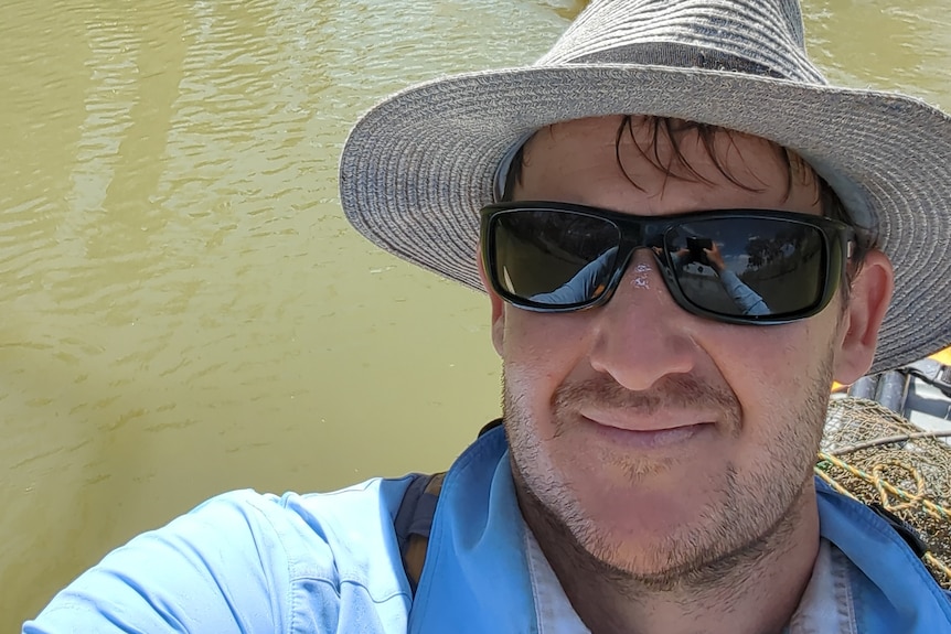 A man in a kayak with a wide brim hat takes a selfie.