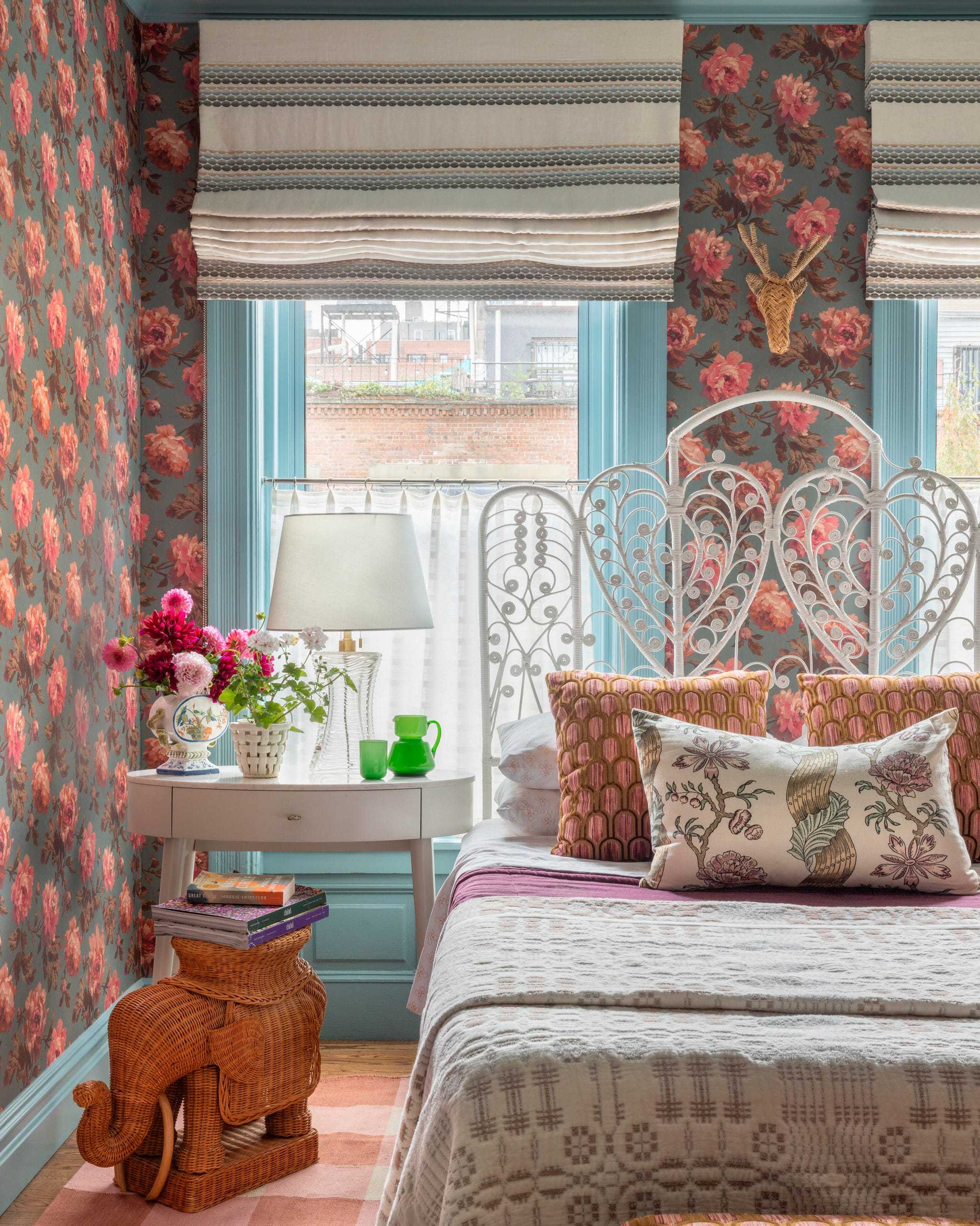 Cozy bedroom with floral wallpaper, decorative pillows, a bedside lamp, and a unique elephant-shaped stool. Cozy bedroom with floral wallpaper, decorative pillows, a bedside lamp, and a unique elephant-shaped stool.