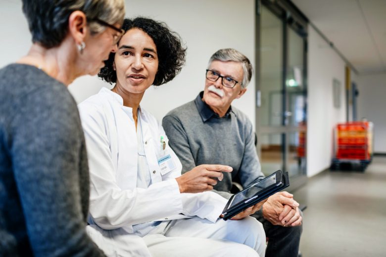 Doctor discusses treatment with an older couple while using a tablet in a hospital.