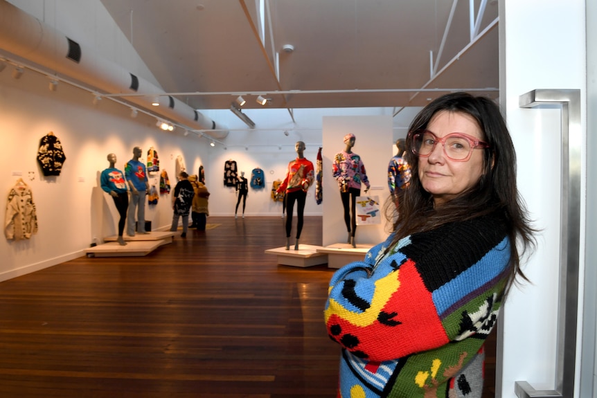 A woman with long black hair, glasses and a brightly coloured jumper at an art exhibition.