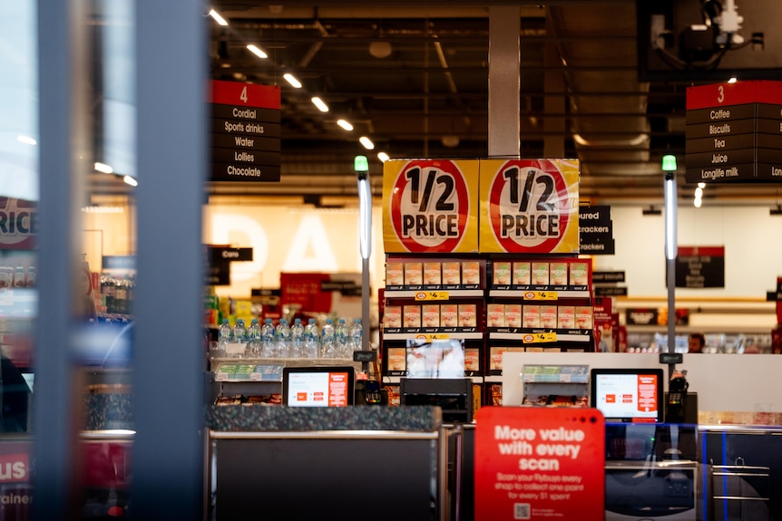 A grocery store with warm lighting, revealed behind automatic glass doors. In the store there's half price signage.