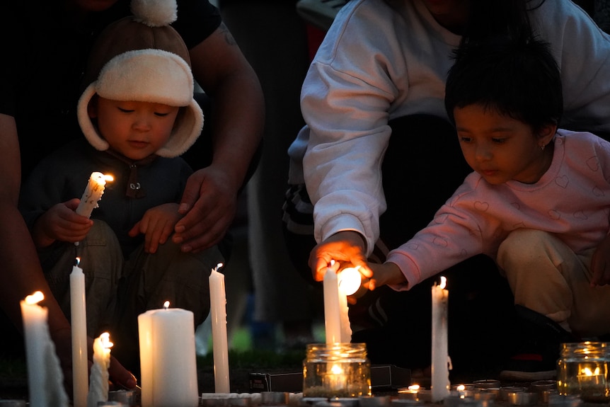 Children holding and lighting candles with the assistance  of some adults.